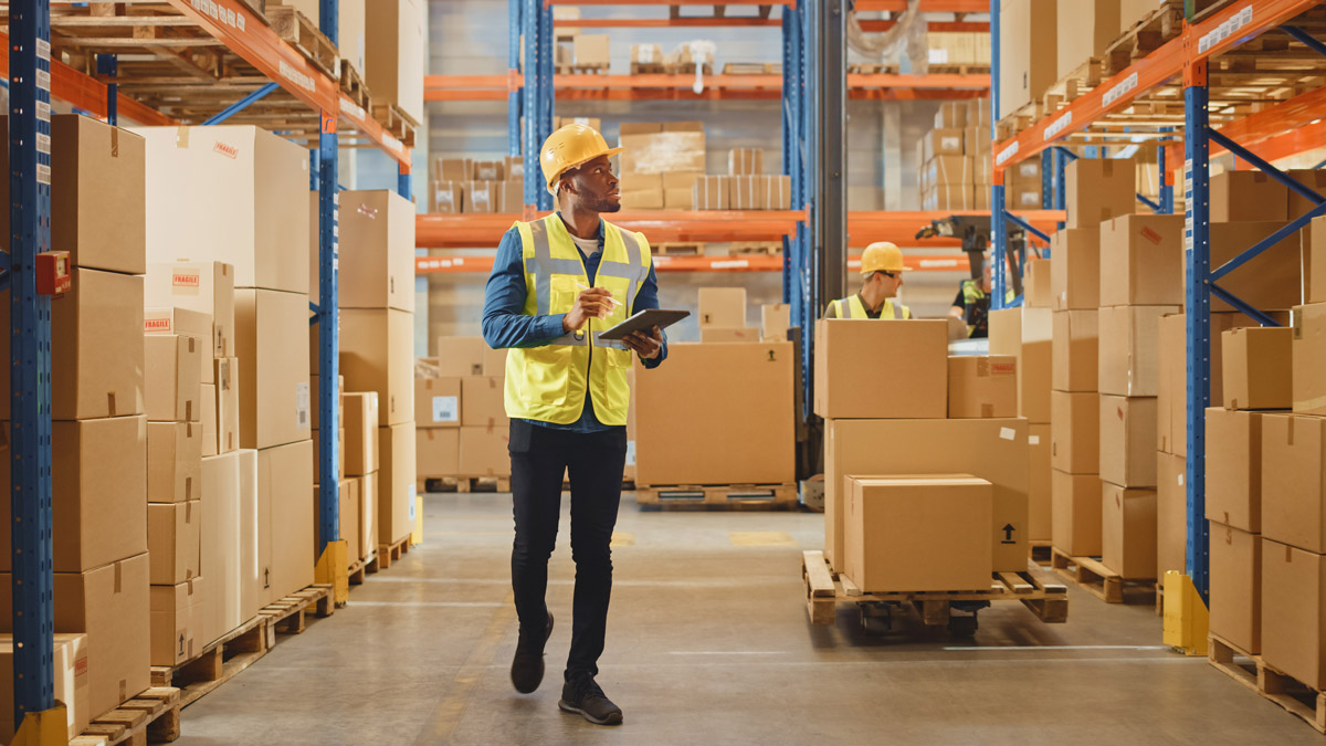 Worker walking through a warehouse checking inventory on a tablet